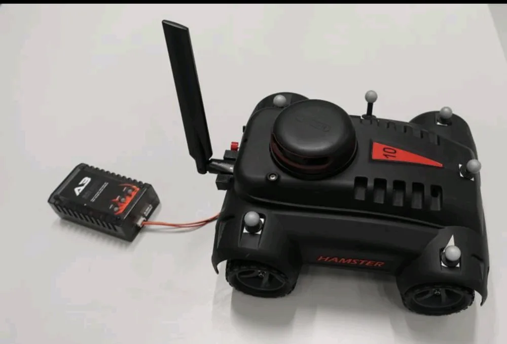 Hamster ground vehicle fitted with reflective OptiTrack markers and an antenna, next to its receiver module
